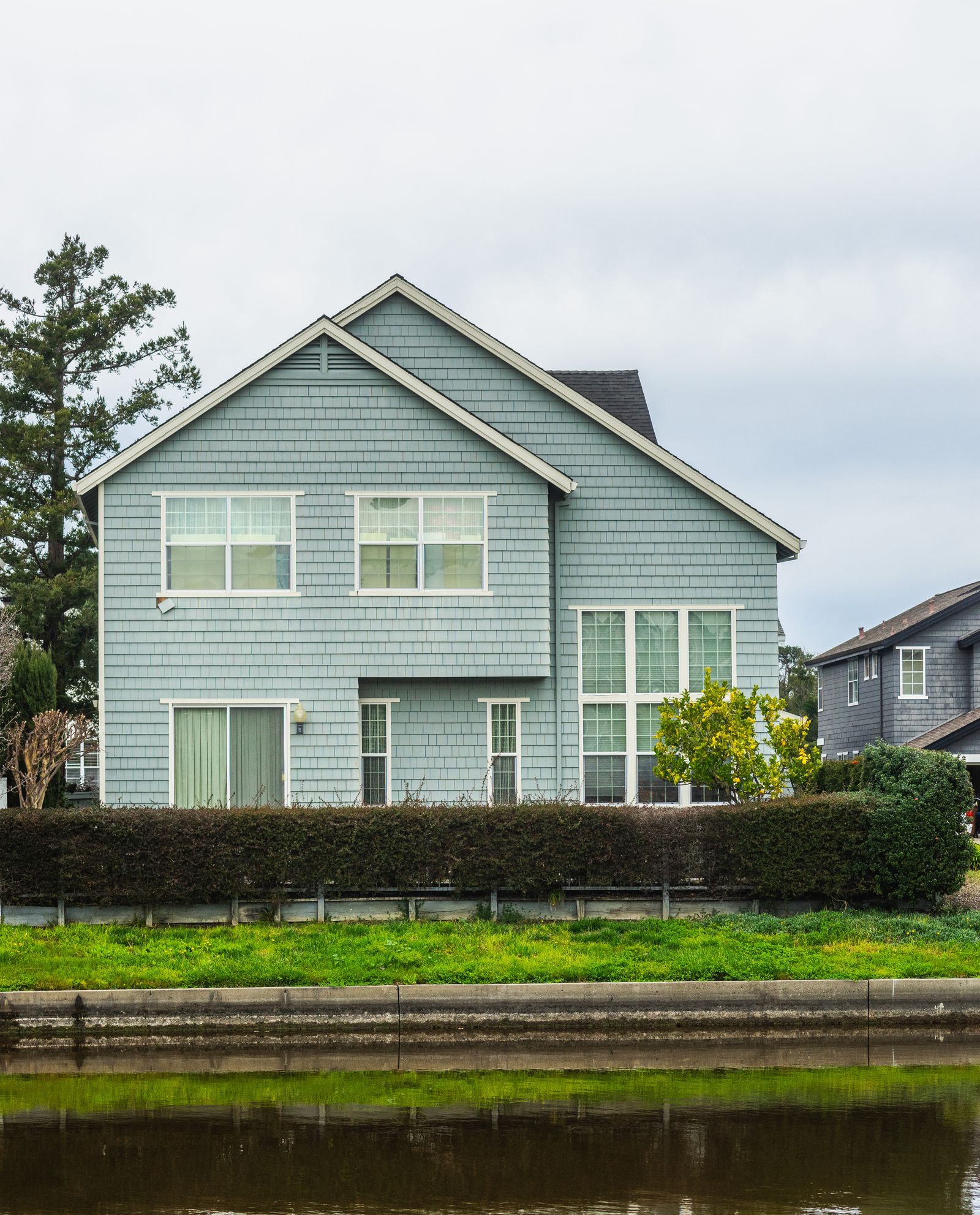 A finished two-storey home with blue-gray siding behind a trimmed hedge